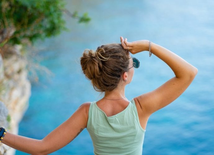 Woman looking out at the blue ocean from a cliff.