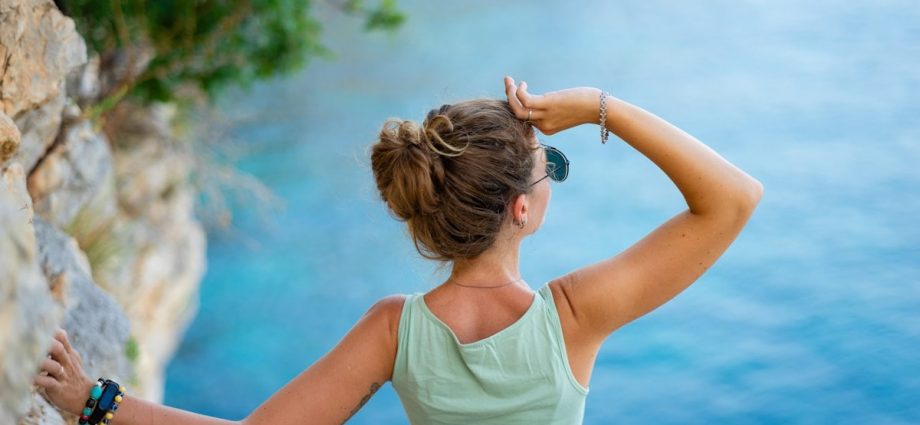 Woman looking out at the blue ocean from a cliff.
